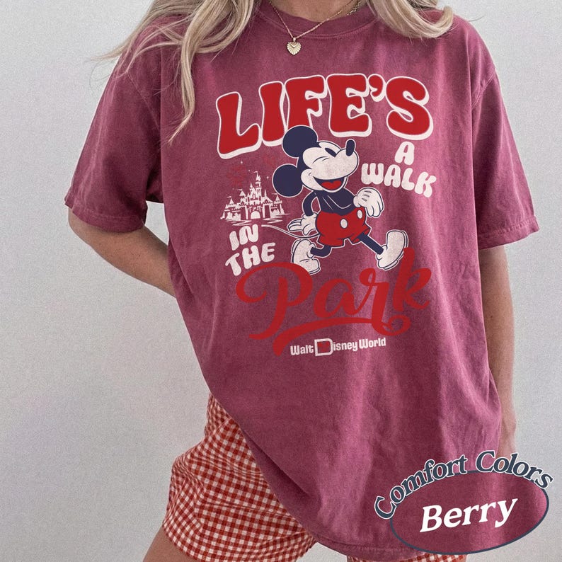 May include: Berry-colored t-shirt featuring Mickey Mouse and the text "LIFE'S A WALK IN THE PARK" with "Walt Disney World" below. The shirt has a vintage look and is made of Comfort Colors material.