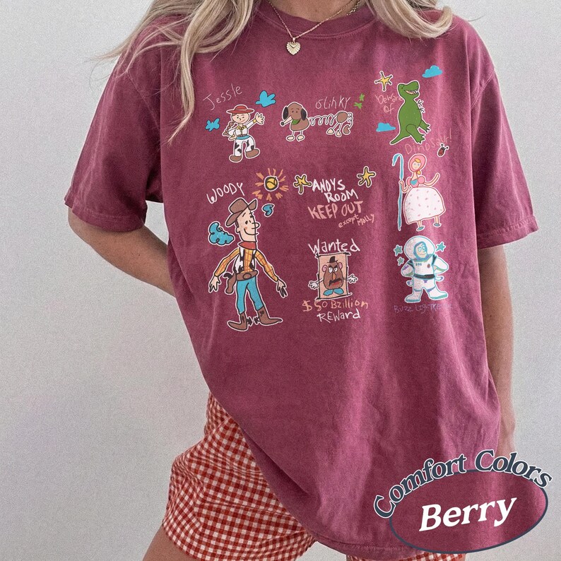 Puede incluir: Camiseta color bayas con personajes de dibujos animados y texto. La camiseta muestra ilustraciones de Woody, Jessie, Slinky Dog, Rex, Bo Peep y Buzz Lightyear. El texto incluye "ANDY'S ROOM KEEP OUT" y "Wanted $50 Billion Reward."