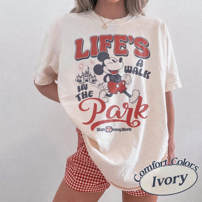 May include: Ivory-colored t-shirt with a retro design featuring Mickey Mouse and the text "Life's a Walk in the Park" in red. The shirt also includes the words "Walt Disney World". The shirt is a Comfort Colors brand.