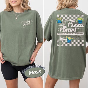 May include: Moss green t-shirt with the Pizza Planet logo on the front and back. The back features the Pizza Planet logo, alien characters, and text that reads "Friday Night Kids Night".