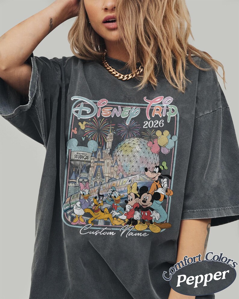 May include: Dark grey t-shirt with a Disney Trip 2026 graphic, showcasing Disney characters, fireworks, and a castle. The shirt includes the text "Custom Name" and "Comfort Colors Pepper".