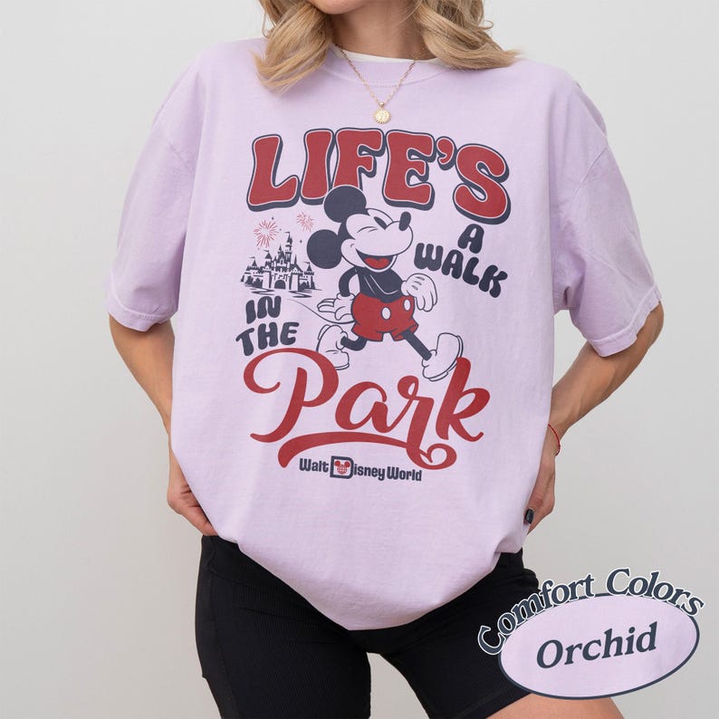 May include: Orchid-colored t-shirt featuring a graphic of Mickey Mouse walking with the text "Life's a Walk in the Park" in red and black. The shirt also includes the Walt Disney World logo.