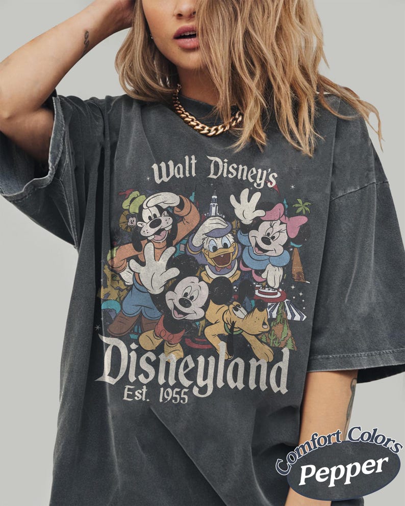 May include: Dark gray t-shirt featuring a vintage Disneyland graphic with Mickey Mouse, Minnie Mouse, Donald Duck, and Pluto. The text reads "Walt Disney's Disneyland Est. 1955". The shirt is a Comfort Colors Pepper tee.
