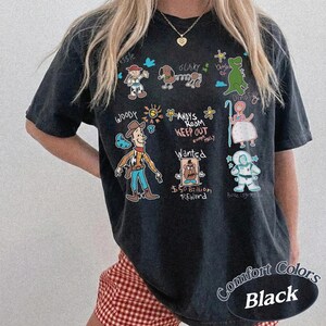 Puede incluir: Camiseta negra con personajes de dibujos animados de una pel&iacute;cula animada popular. La camiseta incluye im&aacute;genes de Woody, Buzz Lightyear y otros personajes, junto con el texto "ANDY'S ROOM KEEP OUT" y "Wanted". La camiseta est&aacute; etiquetada como "Comfort Colors Black".