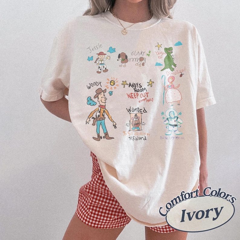 Puede incluir: Camiseta Comfort Colors color marfil con dibujos de personajes de dibujos animados como Woody y Jessie. La camiseta incluye el texto "ANDY'S ROOM KEEP OUT" y "Wanted".
