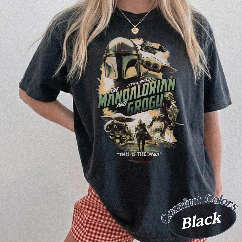 Może przedstawiać: Czarny t-shirt z grafiką z serii Star Wars, "The Mandalorian and Grogu". Projekt zawiera hełm Mandaloriana, Grogu i frazę "This is the Way". Koszulka jest oznaczona jako "Comfort Colors Black".