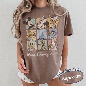 May include: Espresso-colored t-shirt featuring a grid of Disney characters including Mickey Mouse, Minnie Mouse, and Goofy. The shirt has the words "Walt Disney World" printed below the grid and "Comfort Colors Espresso" in an oval.