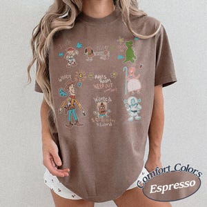 Puede incluir: Camiseta color espresso con dibujos de personajes de Toy Story. La camiseta incluye los textos "Jessie", "Woody", "Andy's Room Keep Out" y "Wanted". La camiseta est&aacute; hecha de material Comfort Colors.