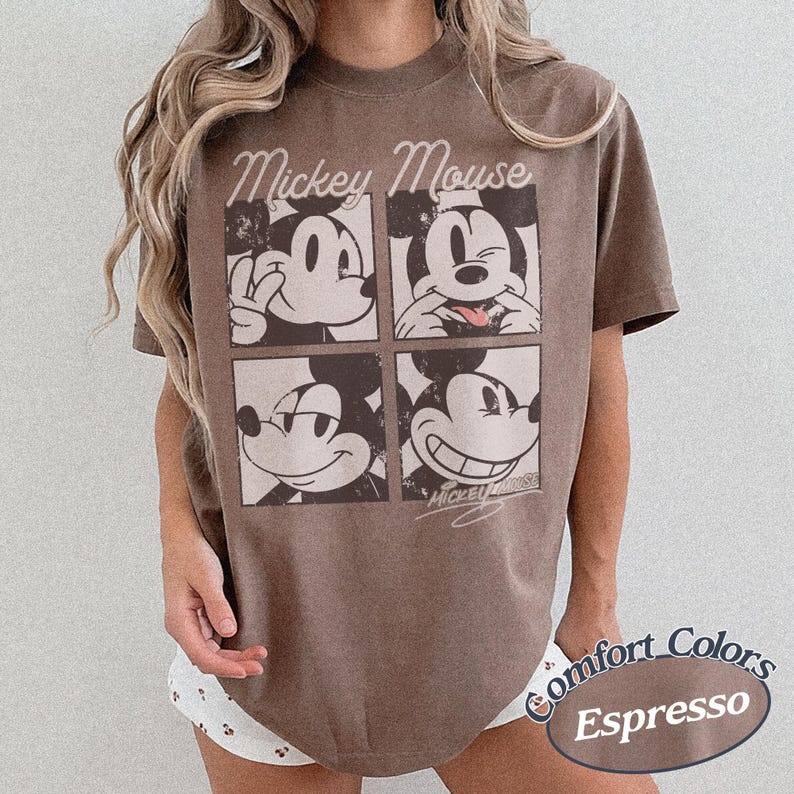 Op de afbeelding: Espresso-kleurig T-shirt met een vierpaneels afbeelding van Mickey Mouse met verschillende gezichtsuitdrukkingen. De woorden "Mickey Mouse" zijn boven de panelen gebogen. Het shirt maakt deel uit van de Comfort Colors-collectie.