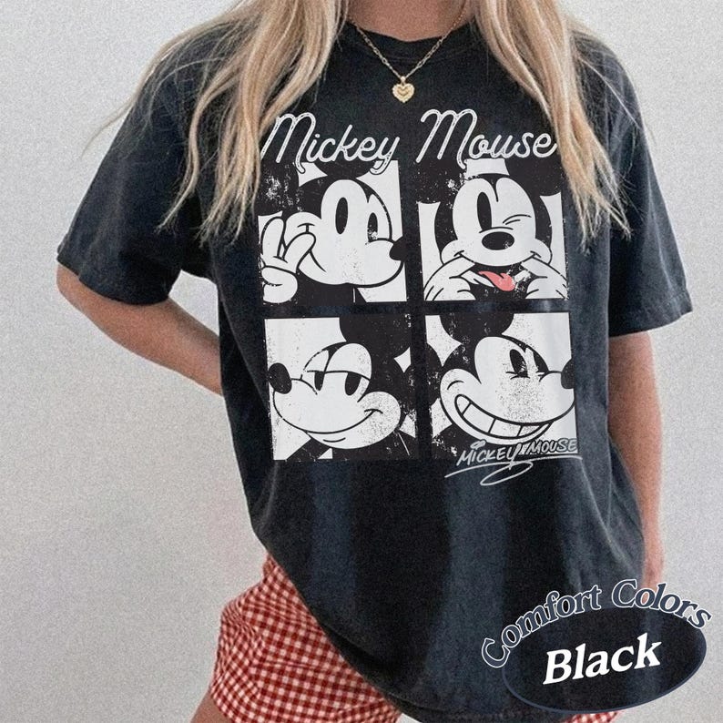 Op de afbeelding: Zwart Comfort Colors T-shirt met een vierpaneels Mickey Mouse-afbeelding. Het ontwerp toont verschillende uitdrukkingen van Mickey Mouse, met de woorden "Mickey Mouse" erboven. Het shirt heeft een relaxte pasvorm.