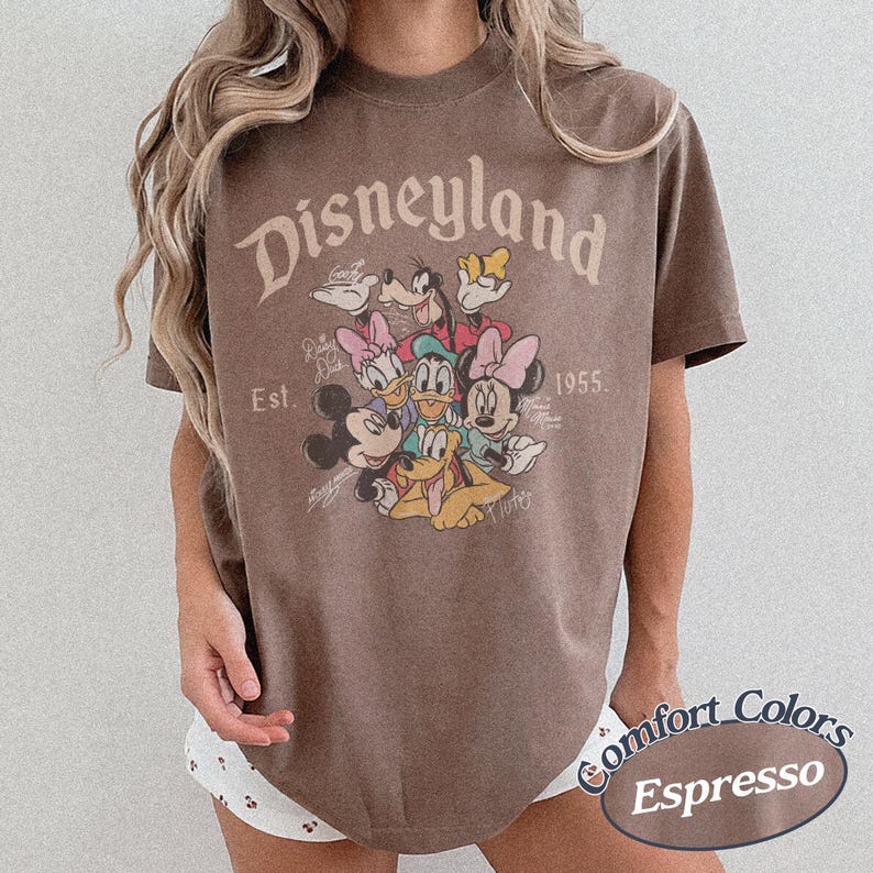May include: Espresso-colored t-shirt featuring a Disneyland graphic with Mickey Mouse, Minnie Mouse, Donald Duck, Daisy Duck, Goofy, and Pluto. The shirt includes the text "Disneyland Est. 1955" and "Comfort Colors Espresso."