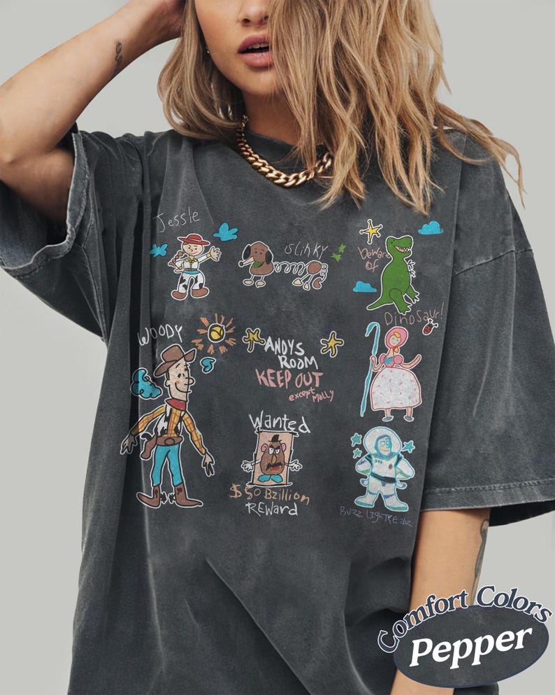 Puede incluir: Camiseta gris oscuro con ilustraciones de dibujos animados de personajes de Toy Story, incluyendo a Woody, Jessie y Slinky. El dise&ntilde;o presenta el texto "ANDY'S ROOM KEEP OUT" y "$50 Billion Reward". La camiseta est&aacute; etiquetada como "Comfort Colors Pepper".