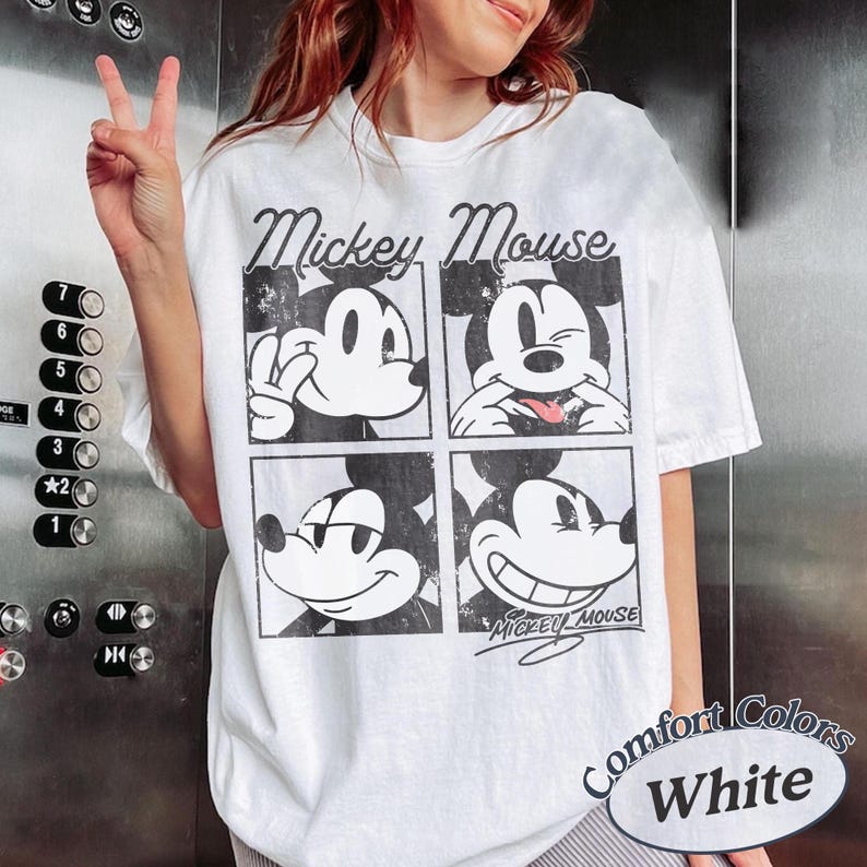 Op de afbeelding: Wit T-shirt met een zwart-wit Mickey Mouse-afbeelding in vier verschillende poses. Het shirt heeft de woorden "Mickey Mouse" boven de afbeeldingen en "Mickey Mouse" in script eronder. Het shirt heeft ook de woorden "Comfort Colors White" rechtsonder.