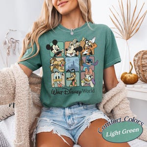 May include: Light green t-shirt featuring a grid of Disney characters including Mickey Mouse, Donald Duck, and Stitch. The shirt has the text "Walt Disney World" and "Comfort Colors" printed on it.