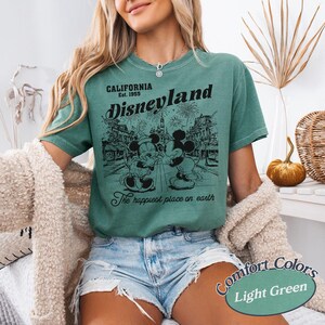 Puede incluir: Camiseta verde claro con un gr&aacute;fico de Mickey y Minnie Mouse frente a Disneyland. La camiseta tiene el texto "CALIFORNIA Est. 1955 Disneyland The happiest place on earth". Parte de la colecci&oacute;n Comfort Colors.