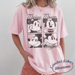 Op de afbeelding: Lichtroze T-shirt met een afbeelding van Mickey Mouse in vier vakken. De woorden "Mickey Mouse" staan boven de vakken en "Comfort Colors Blossom" eronder. Korte mouwen.