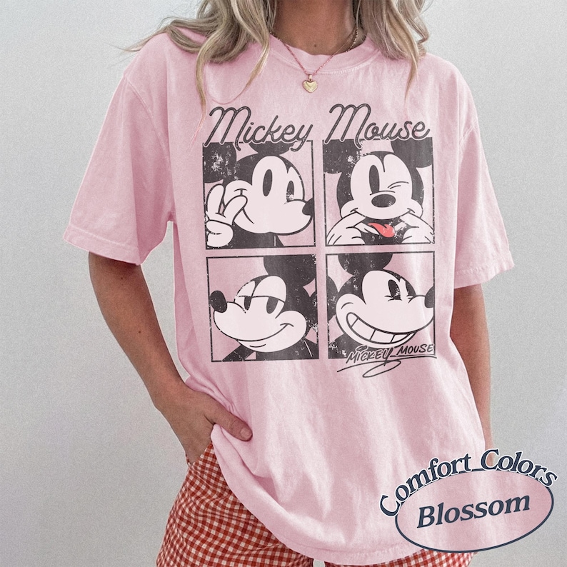 Op de afbeelding: Lichtroze T-shirt met een afbeelding van Mickey Mouse in vier vakken. De woorden "Mickey Mouse" staan boven de vakken en "Comfort Colors Blossom" eronder. Korte mouwen.