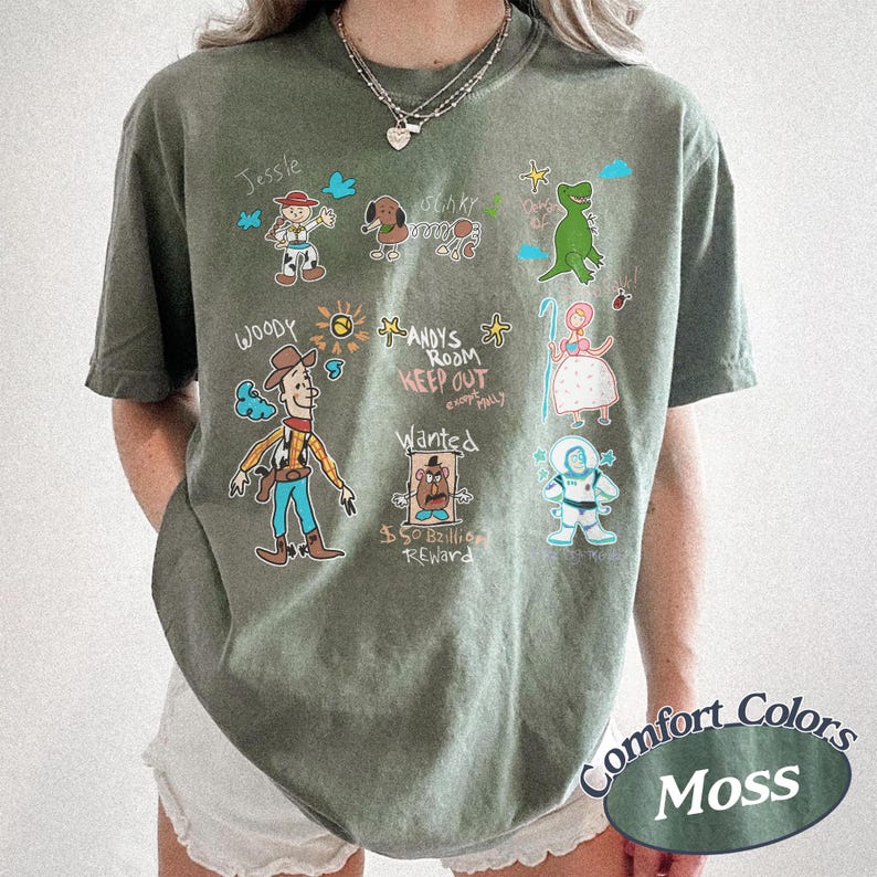 Puede incluir: Camiseta verde musgo con personajes de dibujos animados de Toy Story. El dise&ntilde;o incluye a Woody, Jessie, Slinky Dog, Rex, Bo Peep y Buzz Lightyear. El texto dice "Andy's Room Keep Out" y "Wanted". La camiseta est&aacute; etiquetada como "Comfort Colors Moss".
