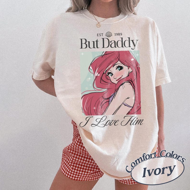 K&ouml;nnte beinhalten: Elfenbeinfarbenes T-Shirt mit einer Comicfigur mit rosa Haaren und dem Text "But Daddy I Love Him". Das Shirt hat auch den Text "EST 1989" und "Comfort Colors Ivory."