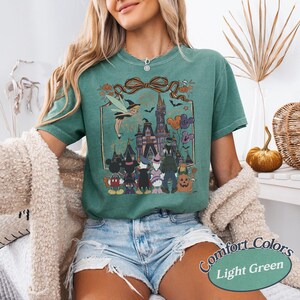 Pode incluir: Camiseta Comfort Colors verde claro com um gr&aacute;fico tem&aacute;tico de Halloween. O design inclui um castelo, personagens e o texto "Comfort Colors Light Green". A camisa tem mangas curtas.