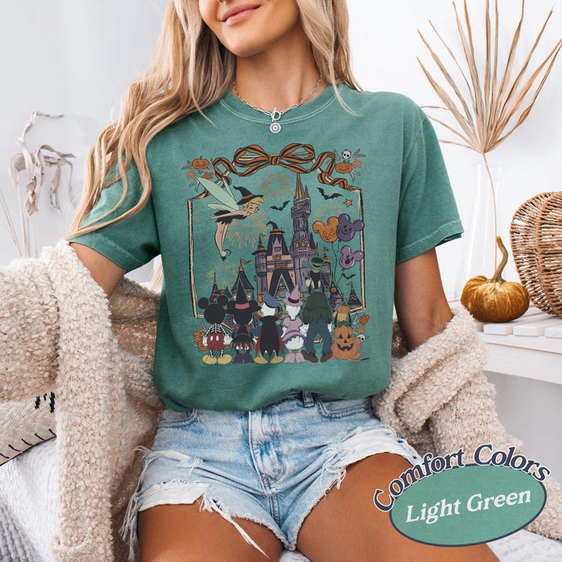 Pode incluir: Camiseta Comfort Colors verde claro com um gr&aacute;fico tem&aacute;tico de Halloween. O design inclui um castelo, personagens e o texto "Comfort Colors Light Green". A camisa tem mangas curtas.
