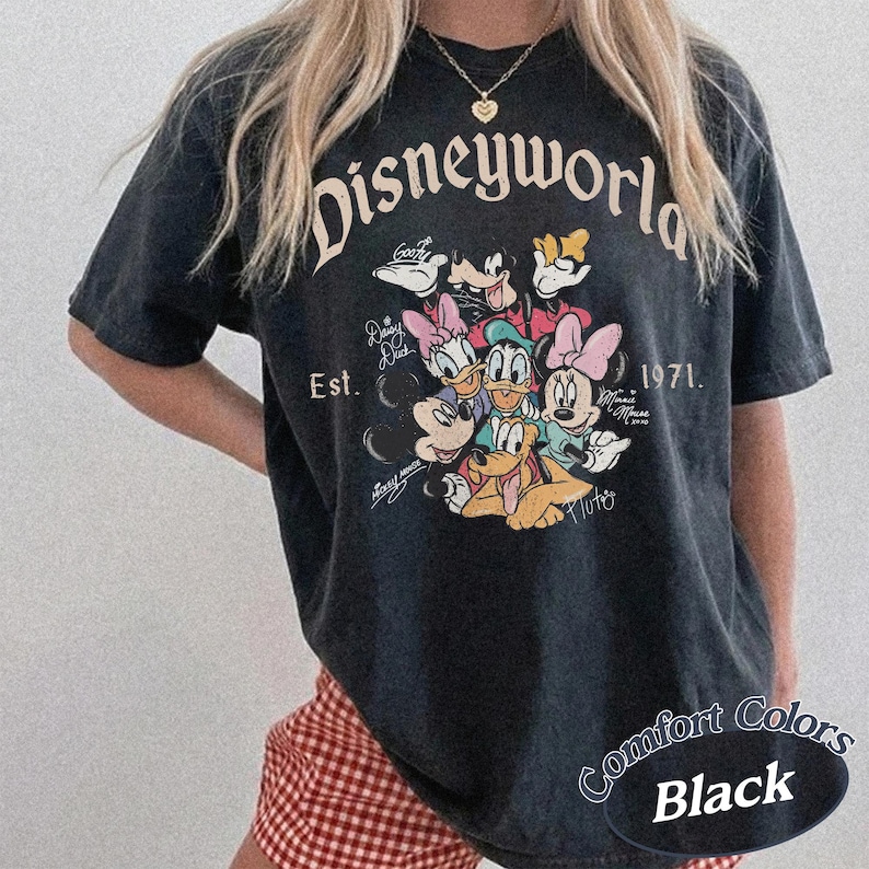 Może przedstawiać: Czarny t-shirt z grafiką Disneyworld z Myszką Miki, Myszka Minnie, Kaczorem Donaldem, Daisy Duck, Goofym i Pluto. Koszulka ma napis "Disneyworld" i "Est. 1971." Koszulka ma r&oacute;wnież napis "Comfort Colors Black."