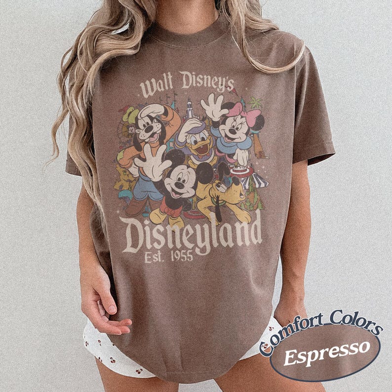 May include: Espresso-colored t-shirt featuring a vintage-style Disneyland graphic with Mickey Mouse, Minnie Mouse, Donald Duck, Goofy, and Pluto. The shirt has the text "Walt Disney's Disneyland Est. 1955" printed on the front.