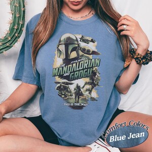 Może przedstawiać: Niebieska koszulka Comfort Colors z grafiką z serii Star Wars, "The Mandalorian and Grogu." Projekt zawiera obrazy Mandalorianina, Grogu i tekst "This is the Way."