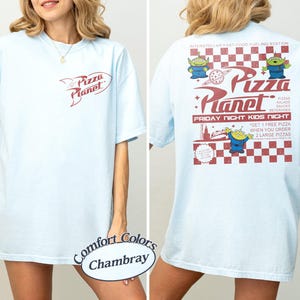 May include: Light blue t-shirt with the Pizza Planet logo on the front and back. The back features the text "Interstellar Fast-Food Fueling Station" and "Friday Night Kids Night" with alien graphics.
