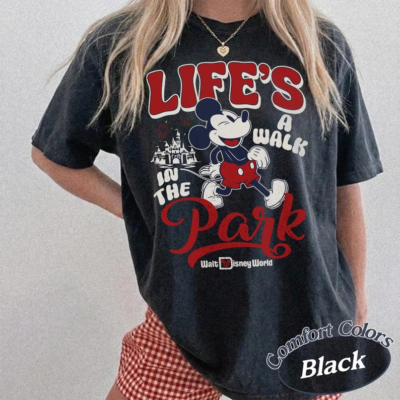 May include: Black t-shirt featuring Mickey Mouse running with the text "LIFE'S A WALK IN THE PARK" in red and white. The shirt also includes the words "Walt Disney World" in red and white.