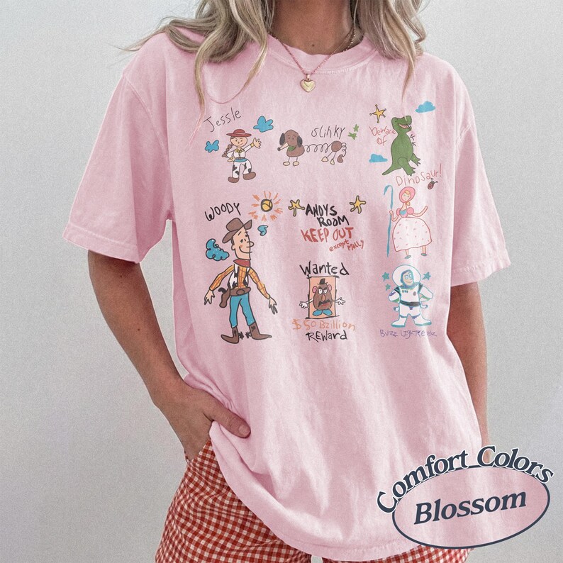 Puede incluir: Camiseta rosa claro con dibujos de personajes de Toy Story y texto. La camiseta tiene el texto "Comfort Colors Blossom" en un dise&ntilde;o circular.