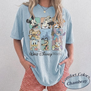 May include: Light blue t-shirt featuring a grid of Disney characters including Mickey Mouse, Minnie Mouse, Chip and Dale, Stitch, Donald Duck, Pluto, and Daisy Duck. The words "Walt Disney World" are printed below the grid. The shirt is labeled "Comfort Colors Chambray".