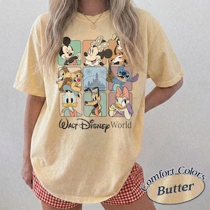 May include: Butter-colored t-shirt featuring a grid of Disney characters including Mickey Mouse, Minnie Mouse, and Stitch. The words "Walt Disney World" are printed below the grid. The shirt is a Comfort Colors brand.