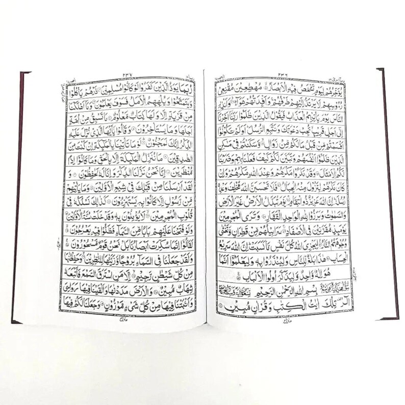 May include: Open book with Arabic script, featuring black text on white pages. The book is open to a double-page spread, with the text filling the pages. The edges of the pages are visible, and the binding is a dark red color.