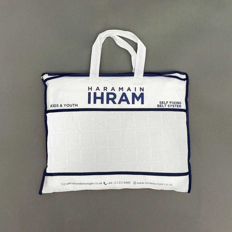 Puede incluir: Bolsa blanca con ribete y asas azul marino. La bolsa muestra el texto "HARAMAIN IHRAM" en azul marino, con "KIDS & YOUTH" y "SELF FIXING BELT SYSTEM" impresos. La bolsa est&aacute; dise&ntilde;ada para ni&ntilde;os y j&oacute;venes.