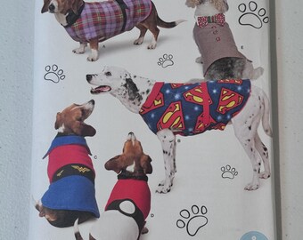 May include: Simplicity pattern 8538 features dog costumes. The pattern includes designs for a superhero, Wonder Woman, and other outfits. The cover shows dogs wearing the costumes, with paw prints scattered around.