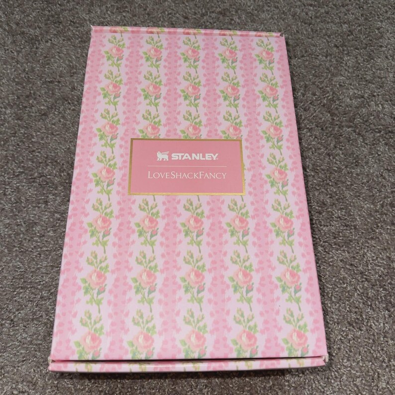 May include: A pink rectangular box with a floral pattern of pink roses and green leaves. The box has a pink label with the text "STANLEY" and "LoveShackFancy" in gold lettering.
