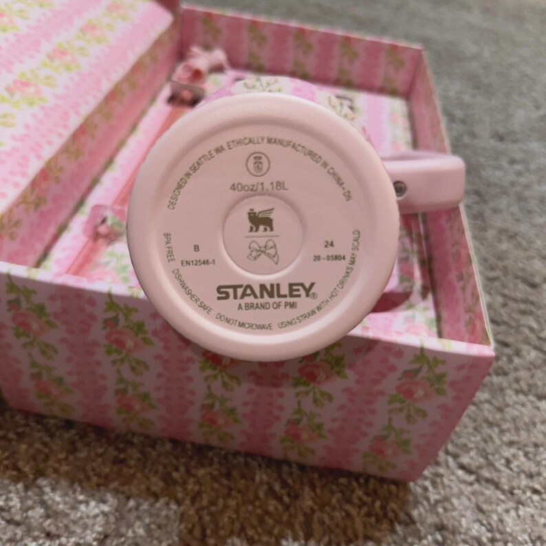 May include: A pink Stanley brand tumbler with a capacity of 40oz/1.18L. The bottom of the tumbler is visible, displaying the brand logo and text. The tumbler is in a pink floral patterned box.