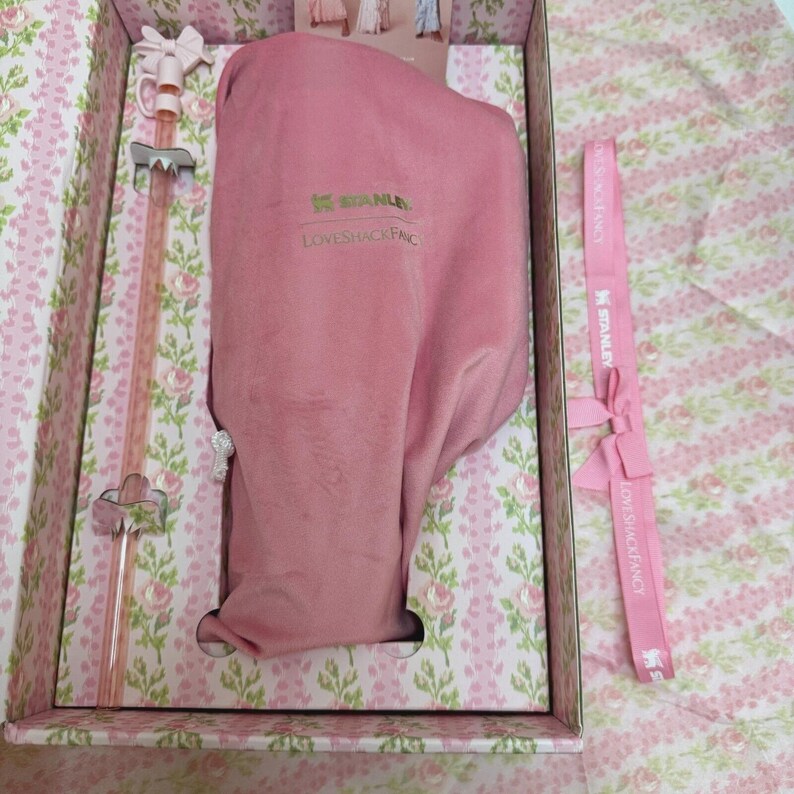 May include: A pink Stanley Loveshack Fancy gift set in a floral patterned box. The set includes a pink insulated bottle, a pink straw, and a pink ribbon with the text "Stanley Loveshack Fancy". The box has a pink and white floral design.