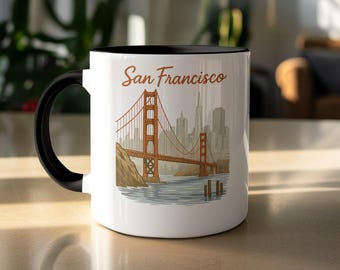 May include: White ceramic mug with a black interior and handle. The mug features an illustration of the Golden Gate Bridge in San Francisco, with the city skyline in the background. The words "San Francisco" are written above the bridge in a brown script font.