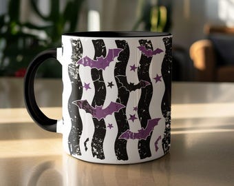 May include: A ceramic mug with a black handle and interior, featuring a white exterior decorated with vertical wavy black distressed stripes, purple bat silhouettes, and small purple stars scattered across the surface of the mug.