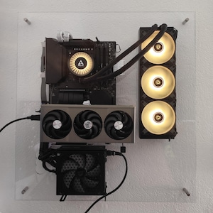 Może przedstawiać: Niestandardowy komputer zamontowany na przezroczystym panelu akrylowym. Zawiera płytę główną, kartę graficzną i chłodzenie cieczą. Wentylatory emitują ciepłe, złote światło. Nowoczesny i elegancki design.