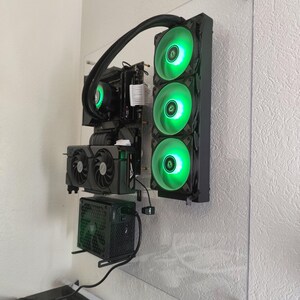 May include: A custom-built computer mounted on a clear acrylic panel. The components include a graphics card, power supply, and a liquid cooling system with three green LED fans. The system is designed for optimal performance and aesthetics.