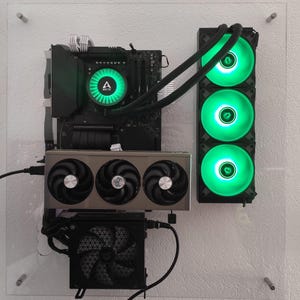 May include: A custom-built computer with a clear acrylic panel. The components include a motherboard, a graphics card with three fans, and a liquid cooling system with three green LED fans. The Arctic logo is visible on the CPU cooler.