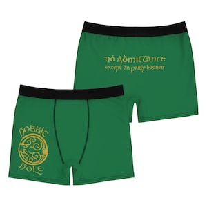 May include: Green boxer shorts with a black waistband. The front features a gold design with the words "Hobbit Hole." The back displays the text "no admittance except on party business" in gold lettering. The shorts are made of a soft, comfortable material.