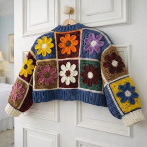 May include: A colorful, crocheted sweater with a patchwork design. The sweater features square panels with various flower designs in yellow, orange, purple, and white. The sleeves and bottom hem are a solid blue, with cream-colored cuffs.