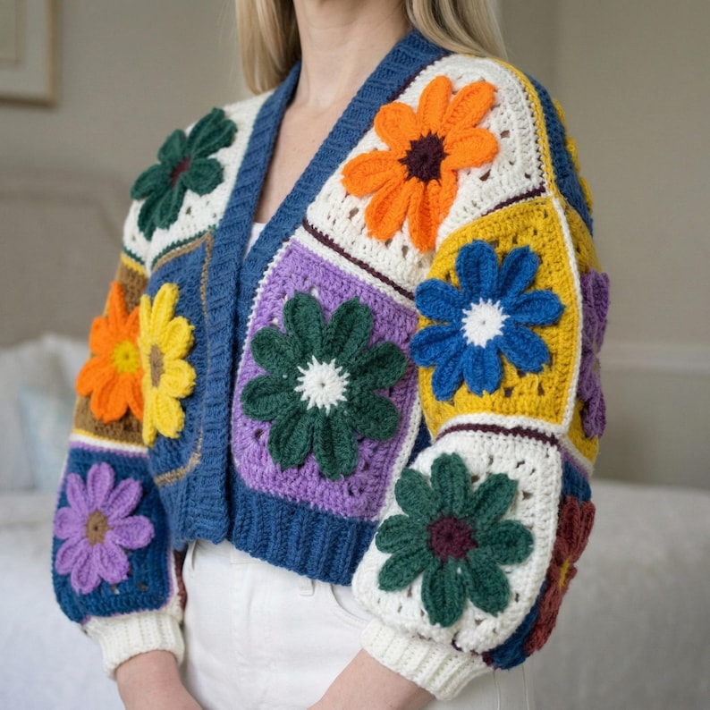 May include: A colorful crochet cardigan featuring a patchwork design with large, three-dimensional flower appliqu&eacute;s. The sweater has a V-neck and long sleeves with ribbed cuffs. The flowers are in shades of orange, yellow, blue, green, and purple, set against a white, blue, and cream background.