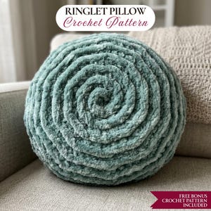 Könnte beinhalten: Ein runder, türkisfarbener Häkelkissen mit Spiralmuster. Das Kissen ist aus weichem, strukturiertem Garn gefertigt und liegt auf einem grauen Sofa. Der Text auf dem Bild lautet "RINGLET PILLOW Crochet Pattern" und "FREE BONUS CROCHET PATTERN INCLUDED."