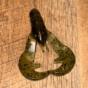 Peut inclure: Un leurre de pêche en plastique souple vert en forme d'écrevisse. Le leurre a un corps segmenté, deux grandes pinces et est parsemé de points noirs. Le leurre est conçu pour attirer les poissons.
