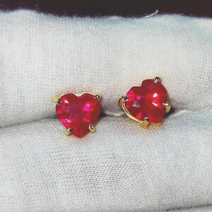Peut inclure: Une paire de boucles d'oreilles en forme de cœur avec des rubis et des montures en or. Les pierres précieuses rouges vives sont taillées en forme de cœur et serties dans une lunette en or. Les boucles d'oreilles sont présentées sur une surface blanche.